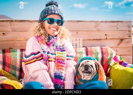 Winter and colorful happy portrait of cheerful beautiful young woman and dog sitting outdoor together - people and animals concept - blue sky in backg Stock Photo