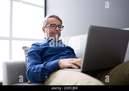 Man Using Laptop Sitting On Couch At Home Stock Photo