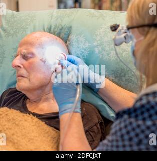 Bedbound elderly man undergoing unpleasant but necessary treatment for long term build up of earwax,compacted over the ear drum and throughout the ear Stock Photo