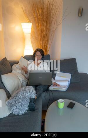 Woman, mid 50s, works from home, with laptop and communicates via headset with colleagues, home office, on the sofa, Stock Photo