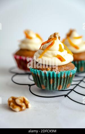 three carrot cake muffins with icing and carrot shaving on a black cooling rack white background Stock Photo