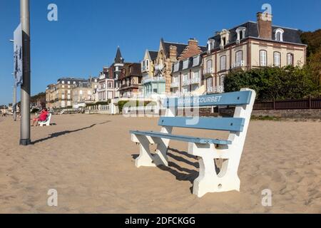 BENCH PAINTED IN WHITE FOR GUSTAVE COURBET ON THE BEACH IN FRONT OF THE OLD BUILDINGS FROM THE EARLY 20TH CENTURY, TROUVILLE-SUR-MER, NORMANDY, FRANCE Stock Photo