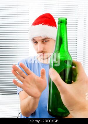 Young Man in Santa Hat refuse a Bottle of the Beer on the Jalousie Background Stock Photo
