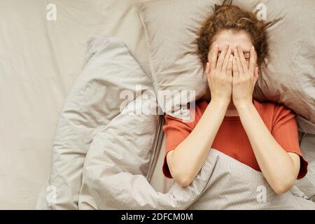 High angle view of young woman covering her face with hands lying on bed Stock Photo