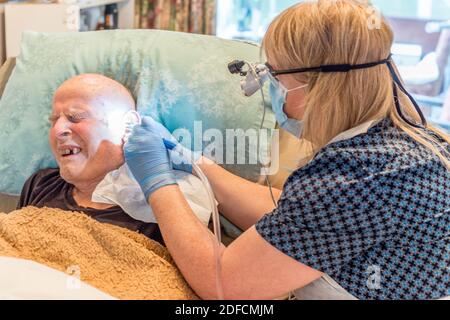 Bedbound elderly man undergoing unpleasant but necessary treatment for long term build up of earwax,compacted over the ear drum and throughout the ear Stock Photo