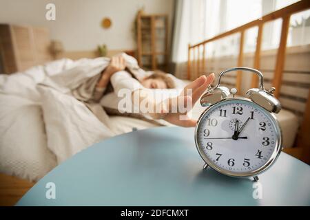 Close-up of alarm clock on the table with woman turning it off in the morning in the bedroom Stock Photo