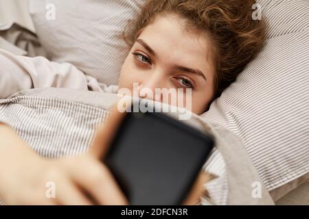 Young woman lying in her bed and talking online using her mobile phone Stock Photo
