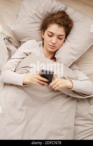 High angle view of young woman using her mobile phone in the morning in her bed Stock Photo