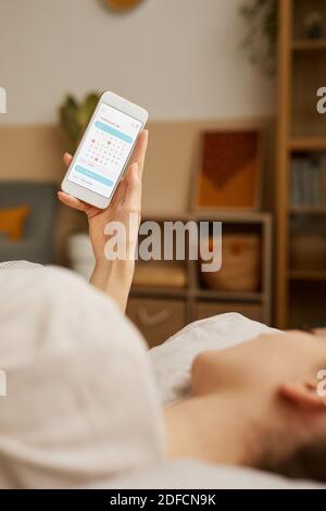 Young woman lying on bed and reading her timetable in calendar on her mobile phone Stock Photo