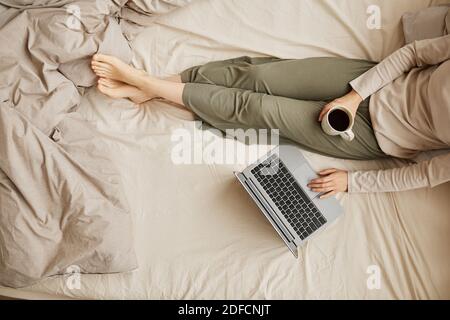 Close-up of woman sitting in her bed with cup of coffee and using laptop computer in the morning Stock Photo