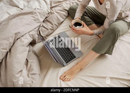 Close-up of young woman sitting in the bed drinking coffee and watching something on laptop computer at home Stock Photo