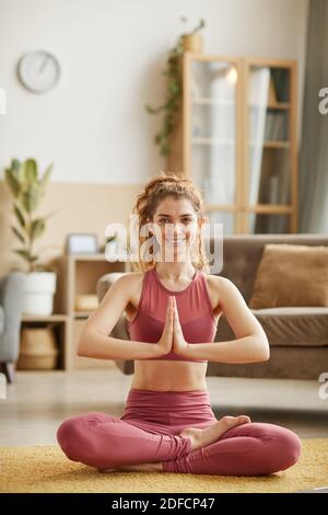 Portrait of young woman smiling at camera sitting on the floor and meditating at home Stock Photo