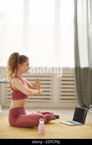 Young healthy woman in sports clothing meditating while watching online yoga lessons on laptop Stock Photo