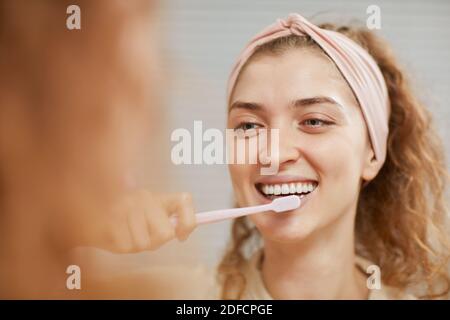 Young woman smiling at camera while cleaning her teeth in the morning Stock Photo