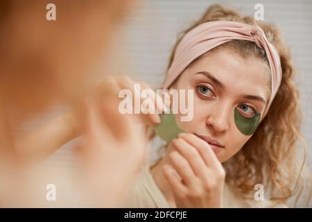 Young woman looking at the mirror while applying patches under her eyes Stock Photo