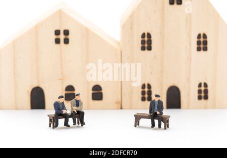 Miniature men are sitting on bench and talking to each other, the background of the house is blurred. Stock Photo