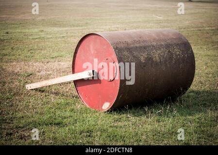 Soil roller laying of the field. Old rusty metal lawn roller on cricket field. Stock Photo