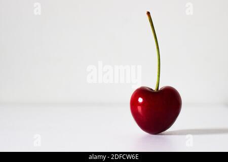 Vibrant single heart shaped cherry with stem isolated on white background. Space for text. Health, nutrition and healthy eating concept Stock Photo
