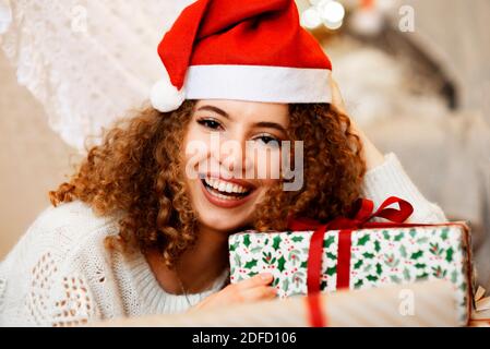 Portrait of pretty lady woman laying on Christmas giftboxes  wear knitted pullover and santa hat on bokeh lights background Stock Photo