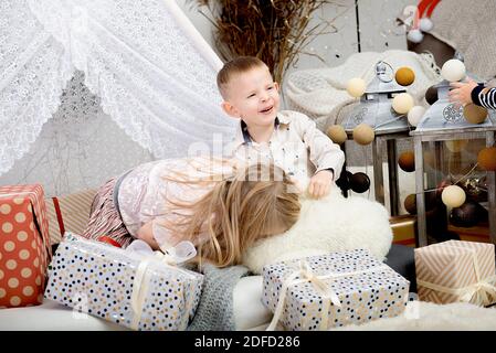 Two funny children kids playing between Christmas gift boxes in a decorated house.Merry Christmas and Happy Holidays! Stock Photo