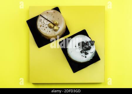 Sweet pastries on display platform top view. Flat lay closeup on a yellow surface, with white and dark chocolate cakes with trim decoration on top. Stock Photo