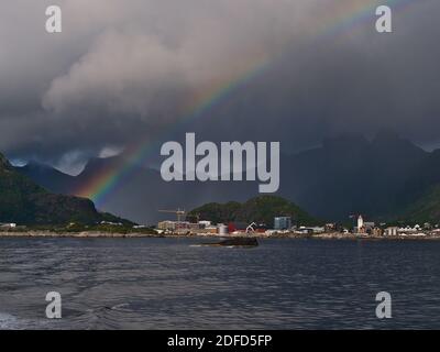 Stunning strong and colorful rainbow above fishing village Svolvær on the coast of Austvågøya island, Lofoten, Norway with rugged mountains and clouds.