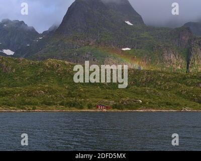 Beautiful rainbow above lonely traditional wooden house with red painted facade on shore of Raftsundet strait on Austvågøya island, Lofoten, Norway. Stock Photo