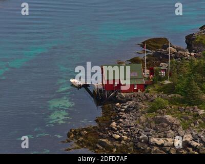 Aerial view of traditional Norwegian wooden rorbu house with stilts and red colored facade on the coast of small island in fishing village Ballstad. Stock Photo