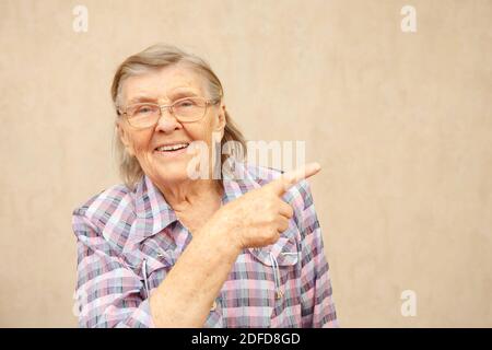 Elderly woman smiles and points to the right side of the frame with empty text space, copy space Stock Photo