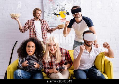 KYIV, UKRAINE - OCTOBER 19, 2020: excited multicultural friends using vr headsets and playing video game during party Stock Photo