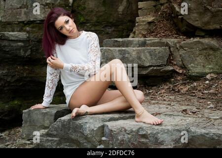 Portrait of a young woman in white, knitted top looking at camera, sitting and posing on rocks, Canada Stock Photo