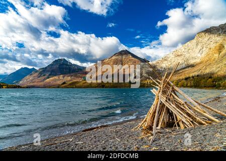 Driftwood Beach, Middle Waterton Lake lakeshore in autumn foliage season morning. Blue sky, white clouds over mountains in the background. Landmarks i Stock Photo