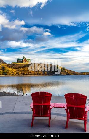 Red chair look over Waterton Lake Marina Point in autumn foliage season sunny morning. Blue sky with colourful clouds reflect on the lake water surfac