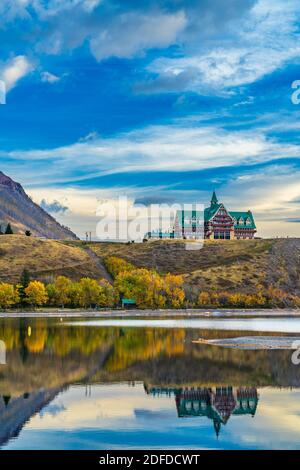 Waterton Lakes National Park lakeshore in autumn foliage season morning. Blue sky, colourful clouds reflect on lake surface like a mirror in sunrise. Stock Photo