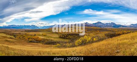Vast prairie and forest in beautiful autumn. Sunlight passing blue sky and clouds on mountains. Fall color landscape background. Waterton Scenic Spot,