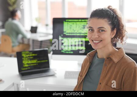 Portrait of professional programmer smiling at camera with computers on the table in the background Stock Photo
