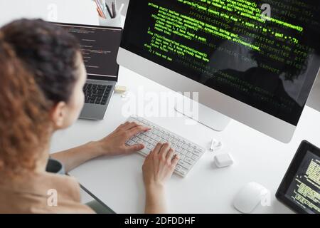 Rear view of programmer upgrading computer system while sitting at the table in front of computer monitor Stock Photo