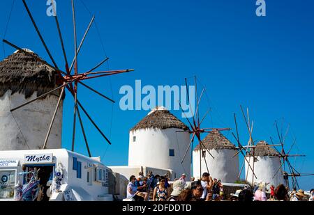 Mykonos, Greece - 10 September 2019: time lapse, tourists near 'Little Venice' admire the sunset. In the background the panoramic windmills.