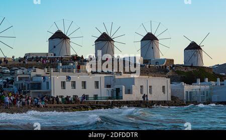 Mykonos, Greece - 10 September 2019: time lapse, tourists near 'Little Venice' admire the sunset. In the background the panoramic windmills.