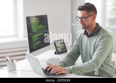 Mature computer programmer programming and coding new technologies while typing on laptop at the table at office Stock Photo