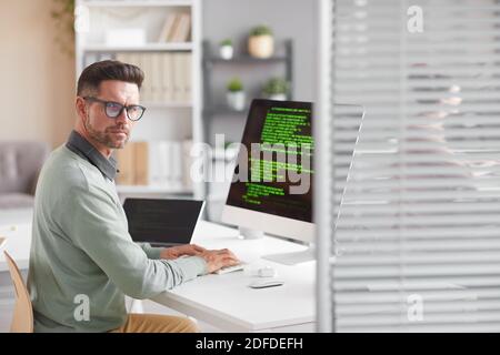 Portrait of mature developer looking at camera while working at the table with computer in software developing company Stock Photo