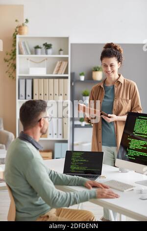 Young woman discussing with her colleague new computer program on computer during working day at office Stock Photo