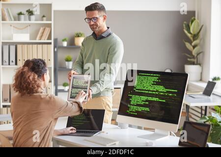 Businessman showing software on tablet pc to his colleague while they working at computer service Stock Photo