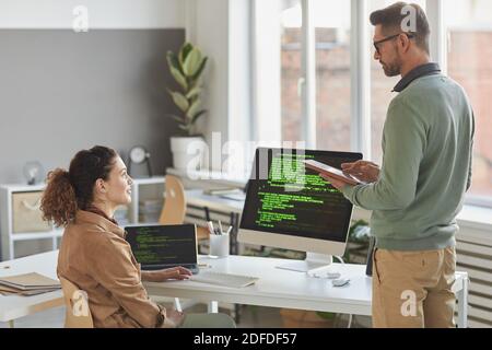 Two computer programmers talking to each other while working with computer system in team at office Stock Photo