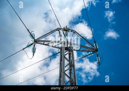 High-voltage insulated wires on glass insulators of power transmission towers against the background of blue sky and white clouds. Stock Photo