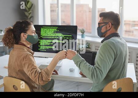 Rear view of two developers in protective masks greeting each other before their work on computers at office Stock Photo
