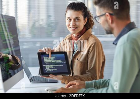 Young woman holding digital tablet and showing new software on the screen to her colleague while they working in team Stock Photo