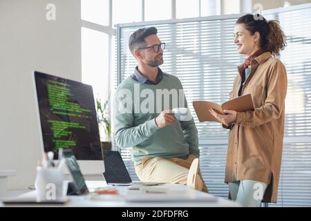 Mobile apps developers discussing work together standing near the table with computer at office Stock Photo