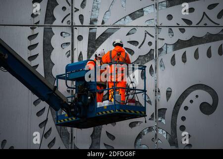 Glasgow, Scotland, UK. 4th Dec, 2020. Pictured: Workmen in PPE high viz orange seen on a cherry picker doing the finishing touches to the M8 Tower - a 131ft high stainless steel structure adorned with the teardrop paisley pattern shape, showcasing a giant electronic advertising display board above the White Cart Viaduct, which will showcase adverts to traffic in north directions. The structure cost more than a million pounds, being funded by Wildstone, the UK's largest outdoor advertising firm. Credit: Colin Fisher/Alamy Live News Stock Photo