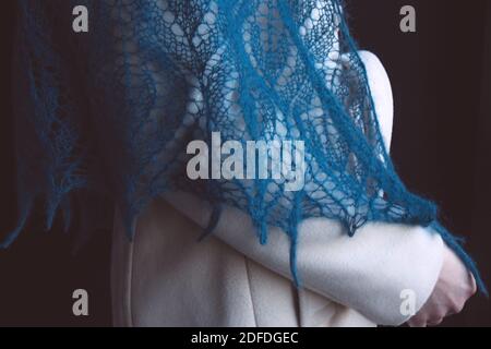 Woman in a light coat and a blue openwork knitted shawl on a black background Stock Photo